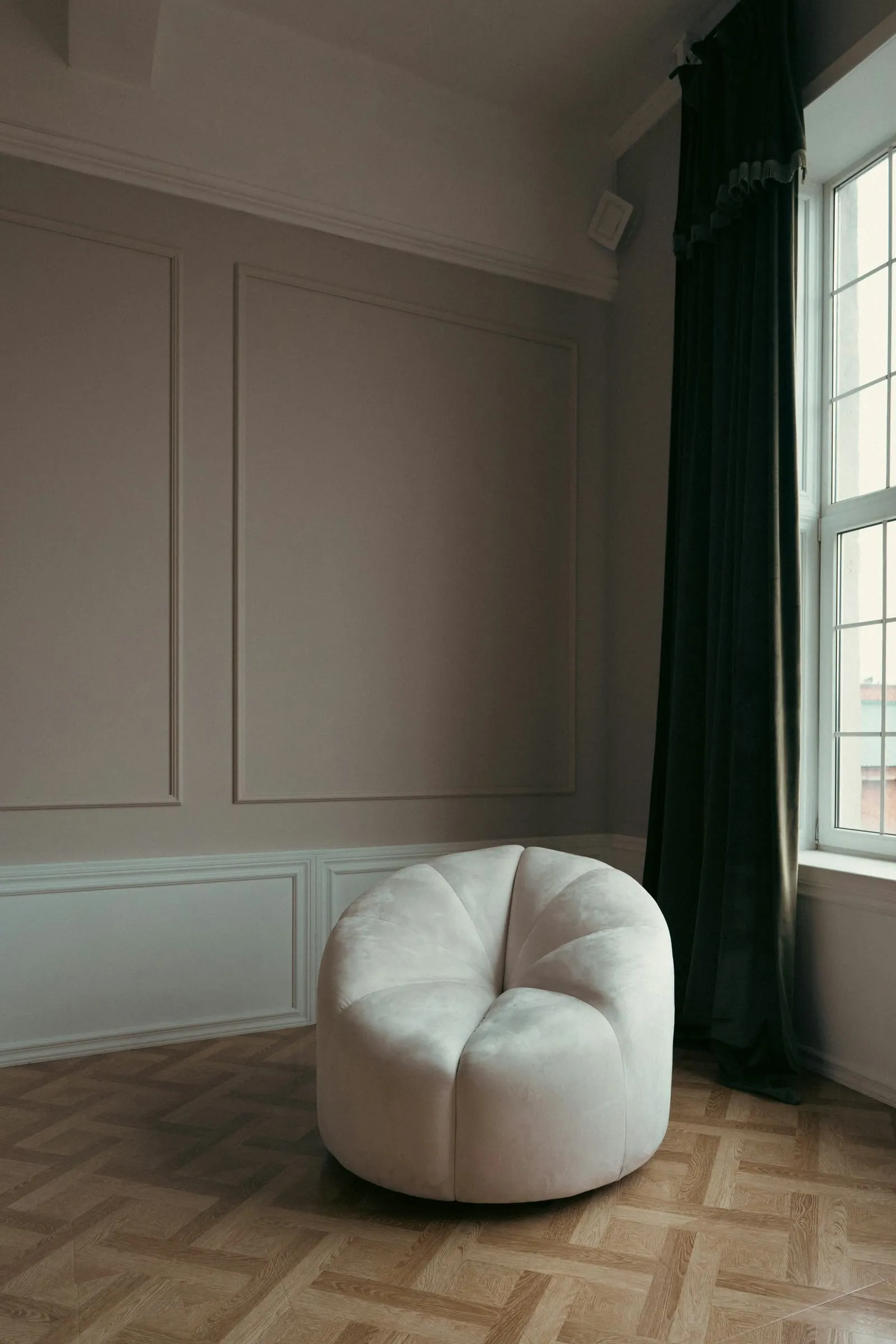 A cream armchair beside a tall window in a quiet room with paneled walls