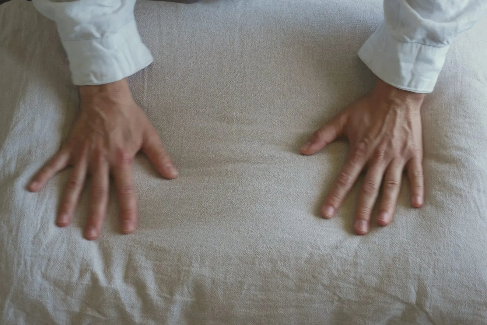 Two hands resting on a textured linen pillow in soft light