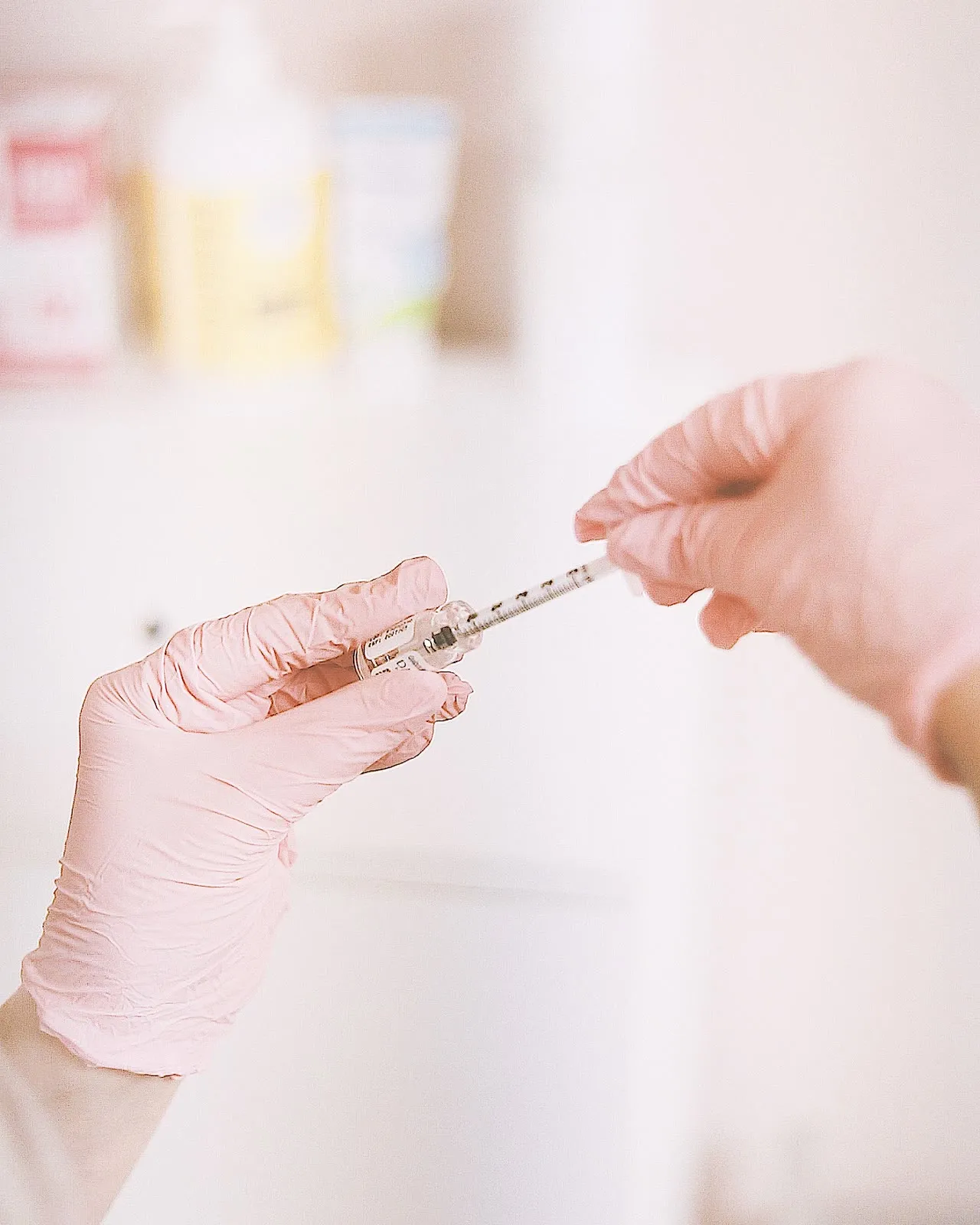 Gloved hands preparing a small syringe in a softly lit treatment room