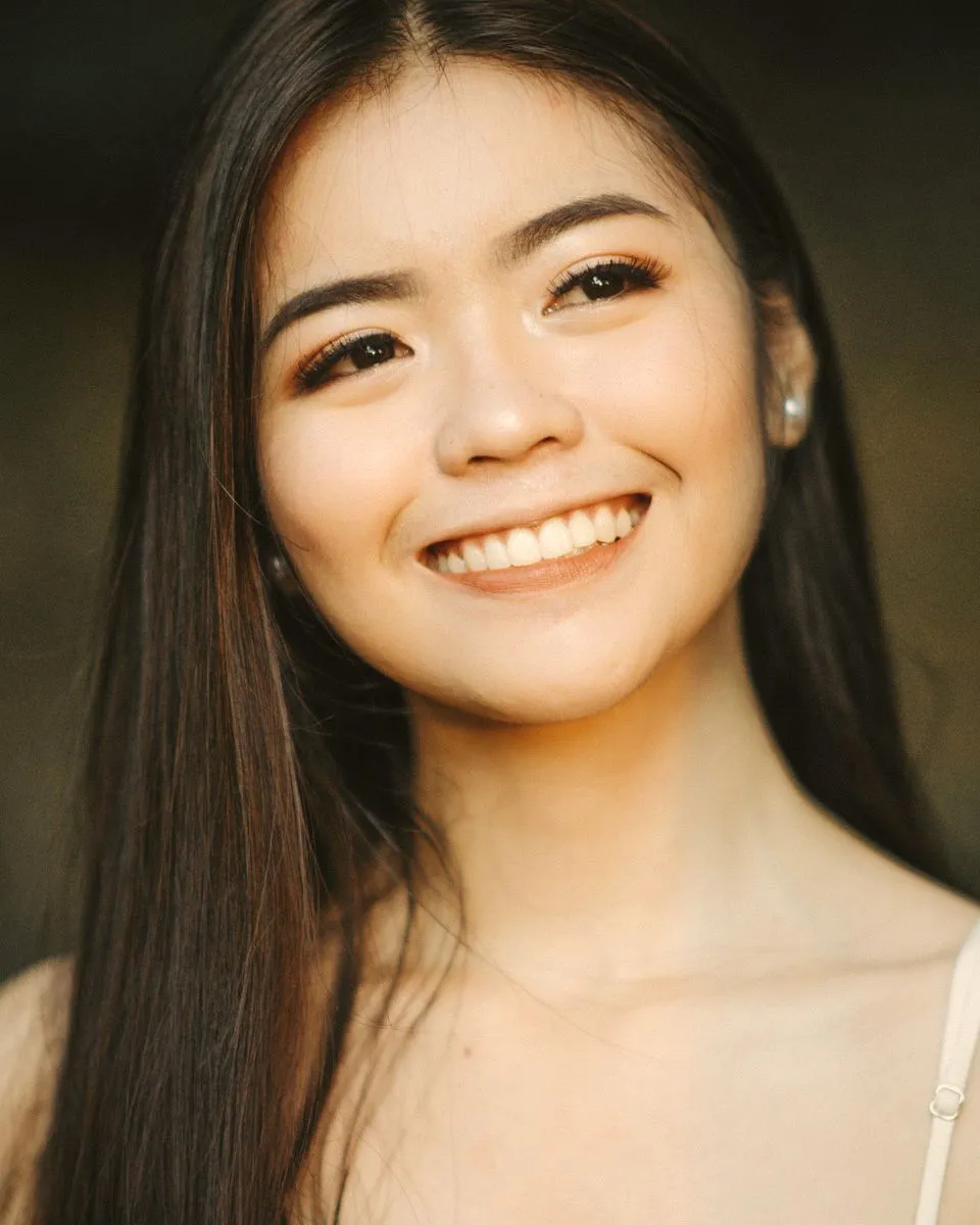 A young woman with long dark hair smiling at the camera in soft warm light