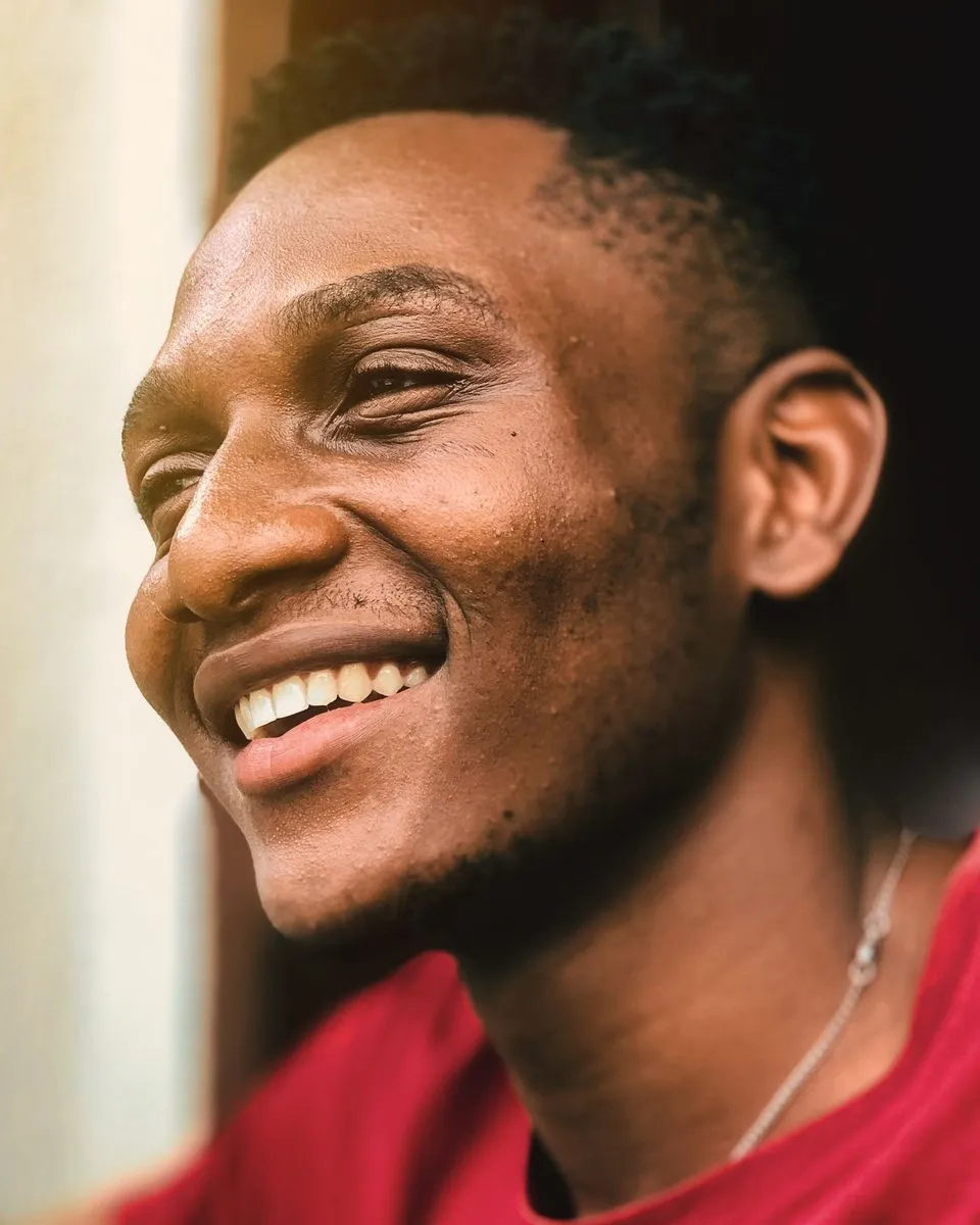 A young man laughing, his face turned toward a bright window