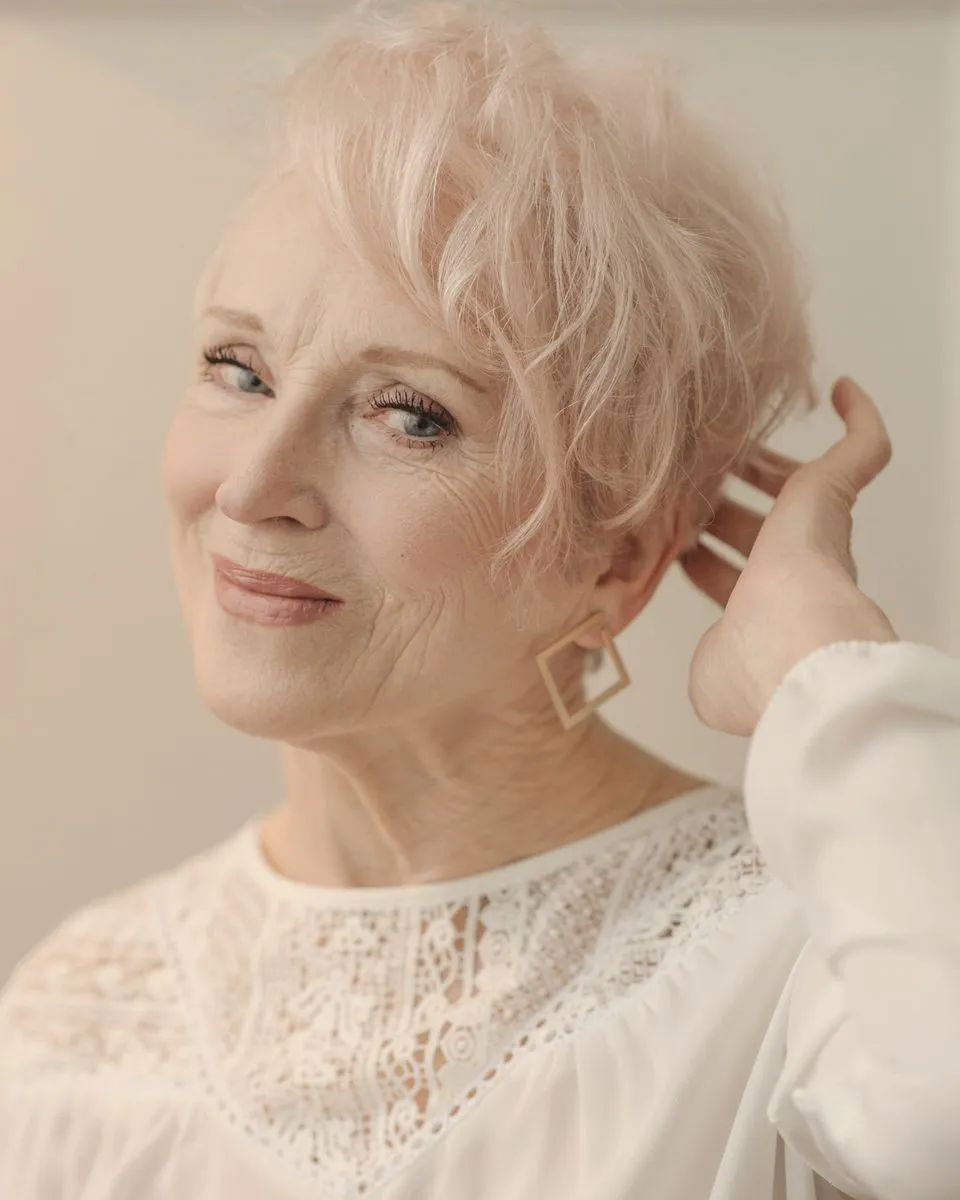 A woman with short silver hair smiling at the camera, one hand resting in her hair